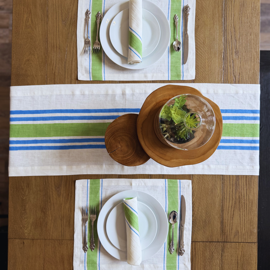 Table setting with green and blue striped linen hand block printed table runner, placemats and napkin and wooden bowls on a wooden table.