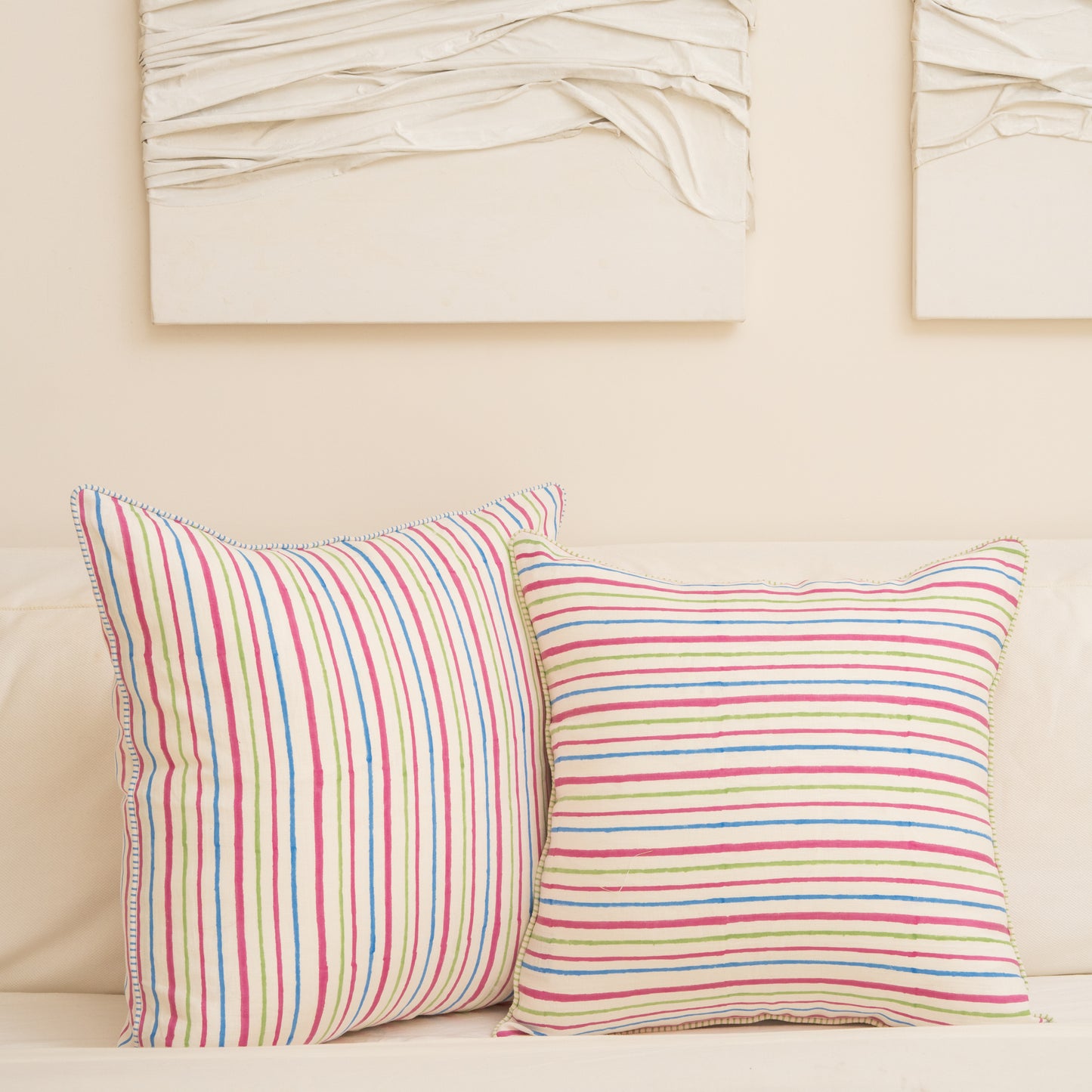 Two Striped with pink, blue, and green lines hand block printed linen pillow cover s in natural dyes placed on a beige sofa with abstract art in the background.