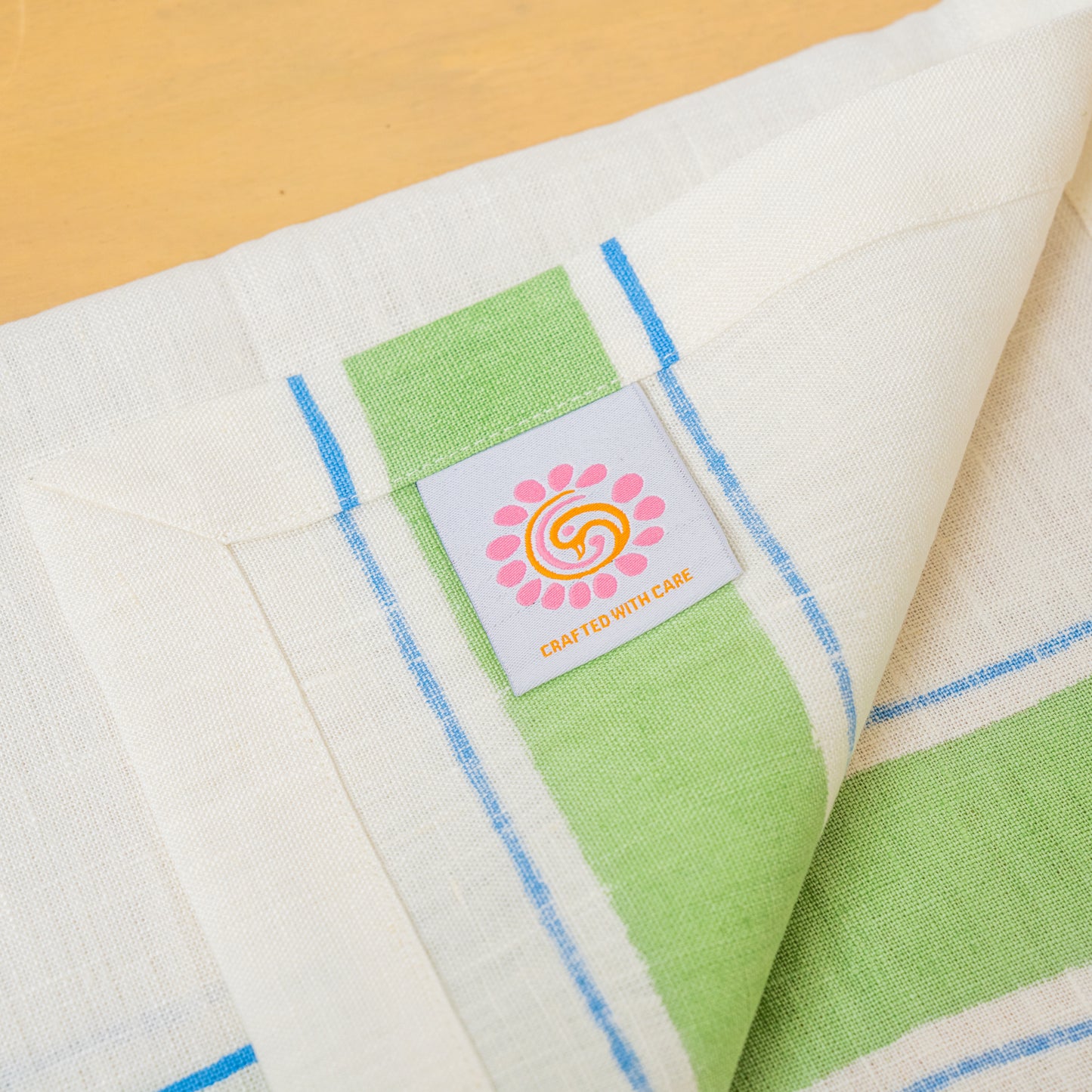 Blue and green striped hand block printed linen placemat with a label, placed on a wooden surface