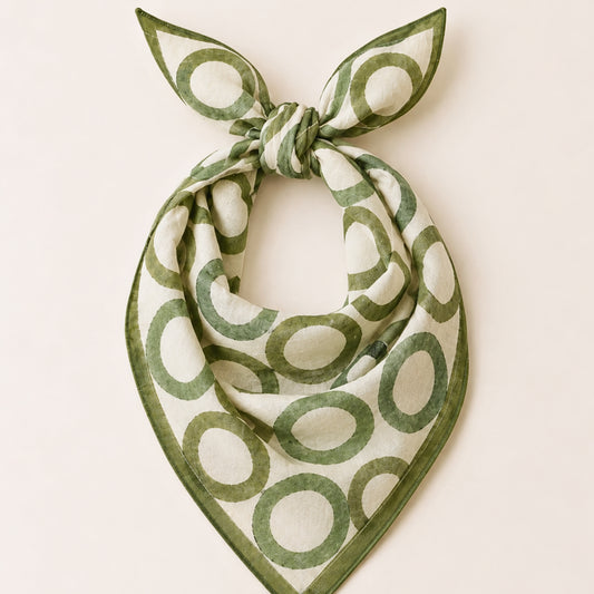A square scarf with a green and off-white circular pattern, tied in a knot at the top and displayed flat against a light beige background.