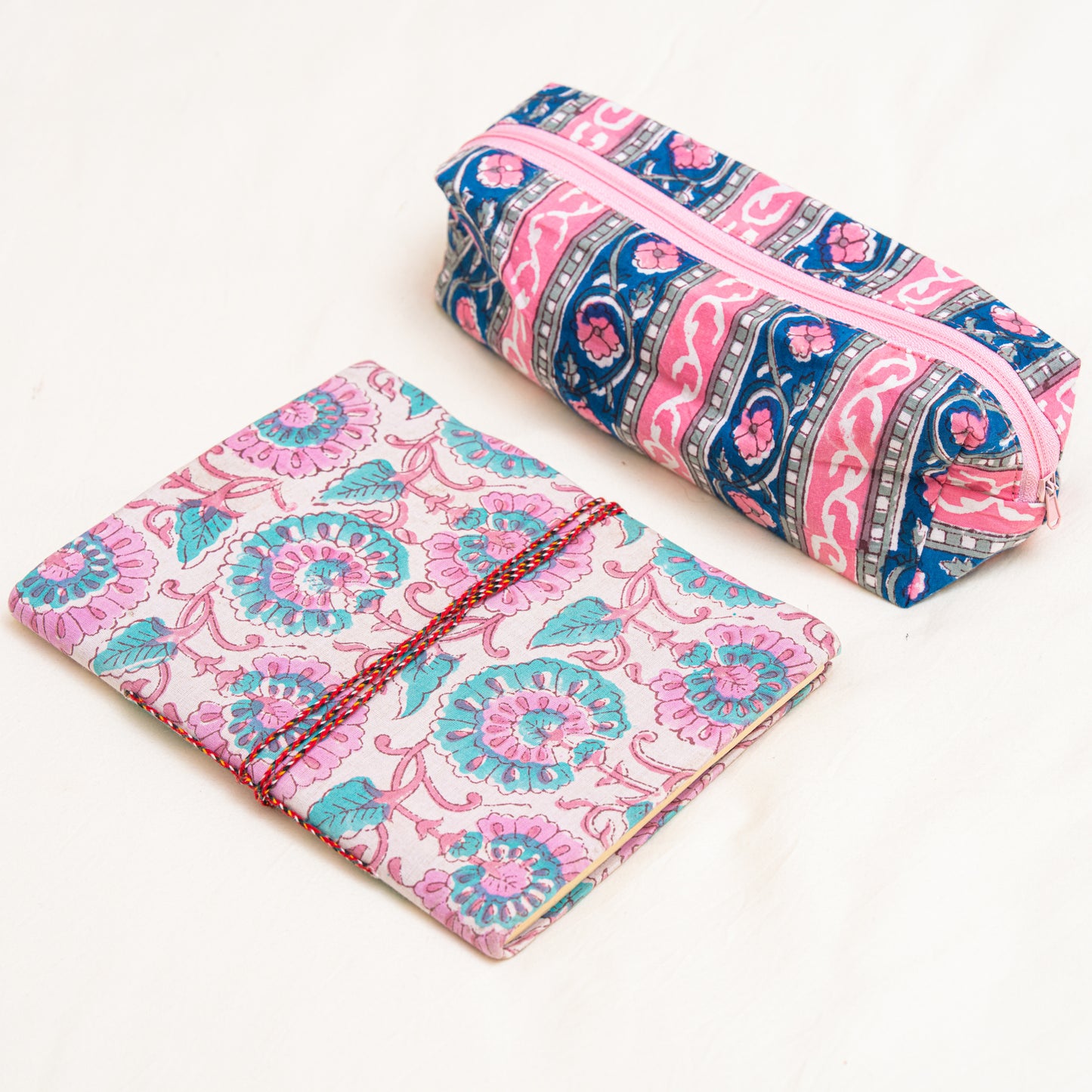 A hand block printed journal and a cotton travel pouch in pink and blue patterns on a white background