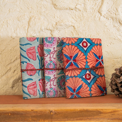 Three patterned notebooks with hand block printed cotton cover , placed on a wooden surface with a stone wall background