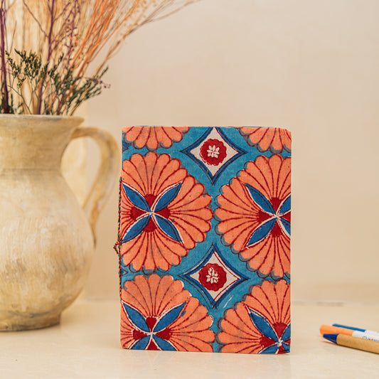 Notebook with a colorful geometric pattern hand block printed on cotton , placed on a wooden surface with a vase and pen.
