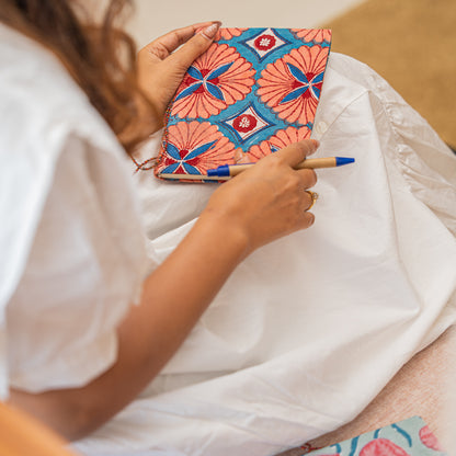 Person holding a colorful notebook with hand block printed cotton cover and pen on a white surface