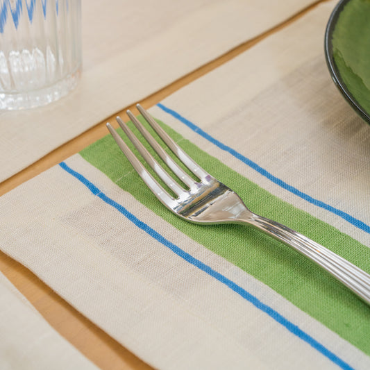 Silver fork on a green and blue striped hand block printed linen placemat with a glass and bowl in the background.