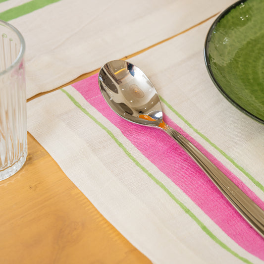 Silver spoon on a pink and green striped hand block printed linen placemat with a glass and bowl in the background