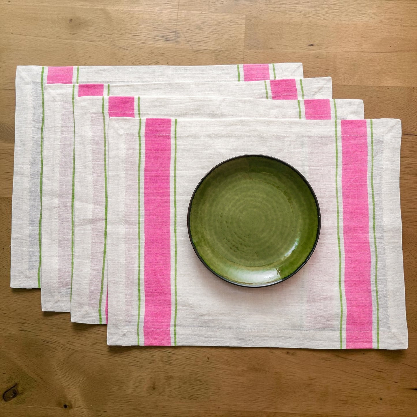 Set of four pink and green striped hand block printed linen placemats with a green bowl on a wooden surface