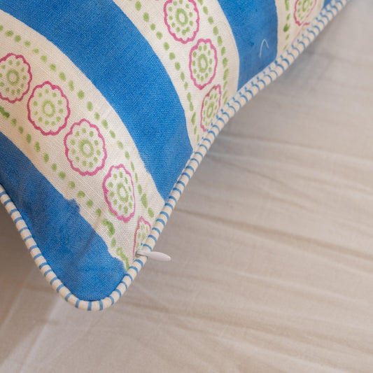 Close-up of a Hand block printed linen pillow cover with blue stripes and floral motifs in natural dyes placed on  a wooden surface