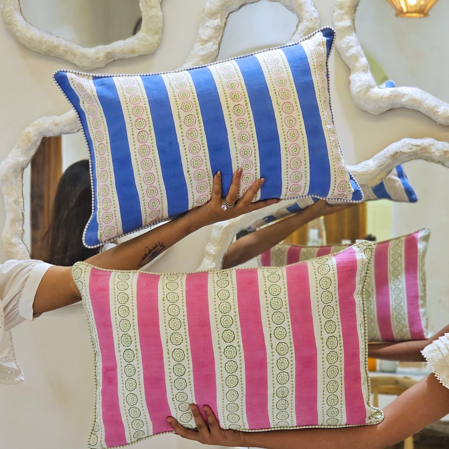 Two striped pillows, one blue and white, one pink and white, held by a person.