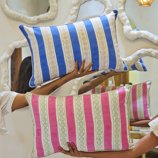 Two striped pillows, one blue and white, one pink and white, held by a person.