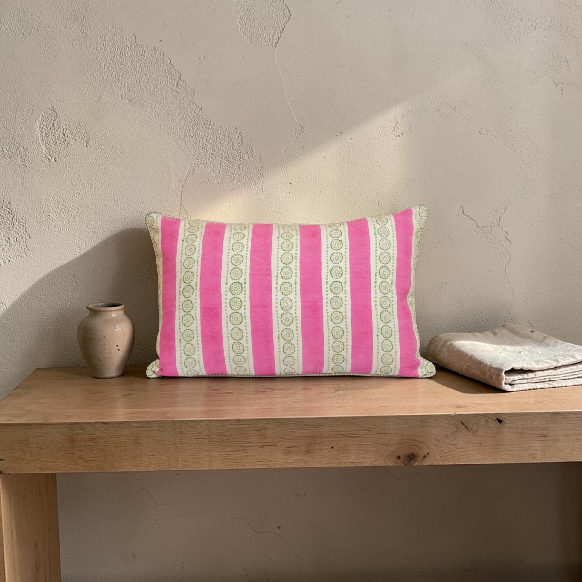 Hand block printed linen pillow cover with pink stripes and floral motifs in natural dyes placed on  a wooden table against a textured wall.