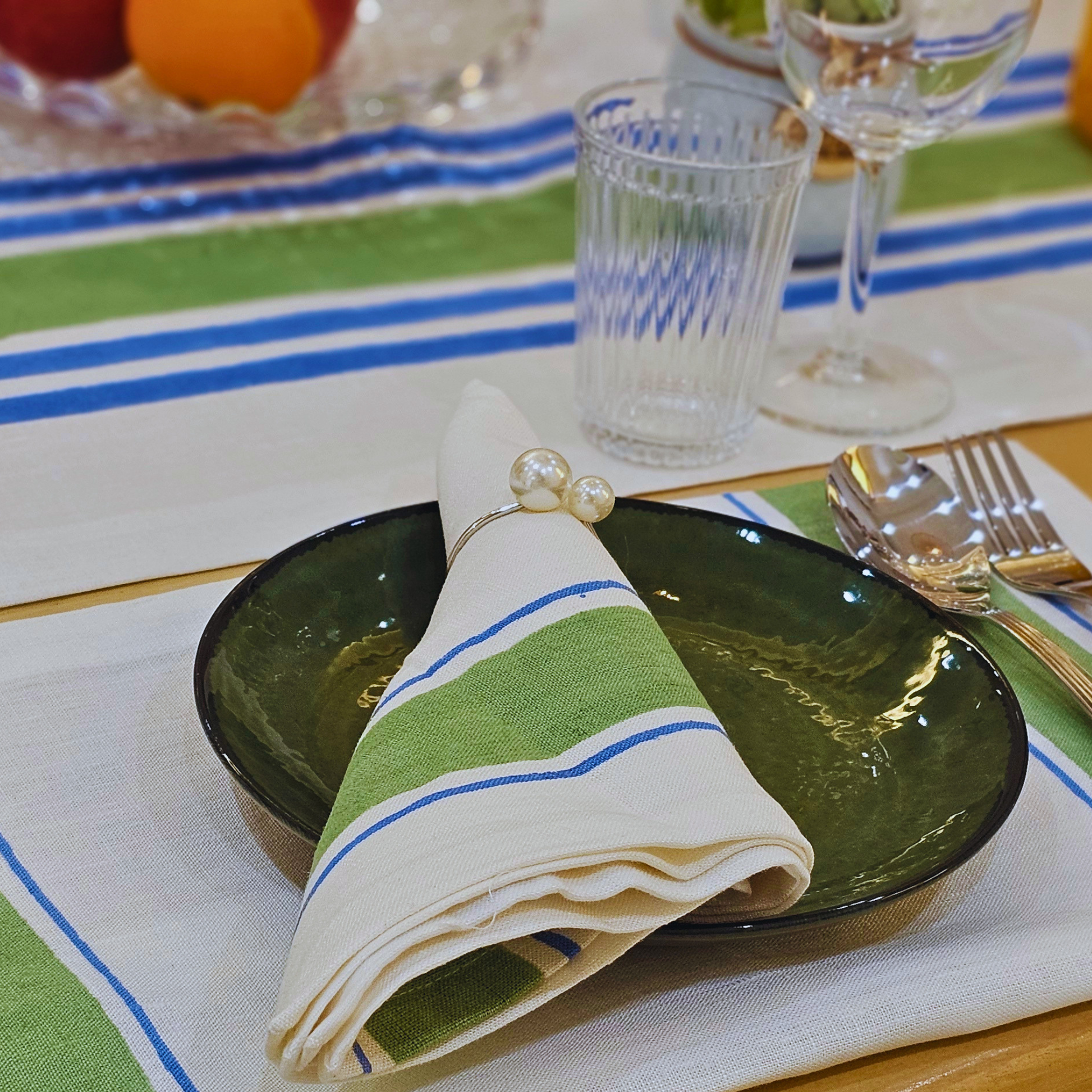 Table setting with green plates, striped napkin, and cutlery on a green and blue striped hand block printed linen tablecloth.