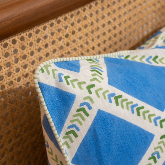 Close-up of a cushion Hand block printed linen pillow cover with interlocking geometric green and blue chevron  print in natural dyes placed on on a wicker chair.