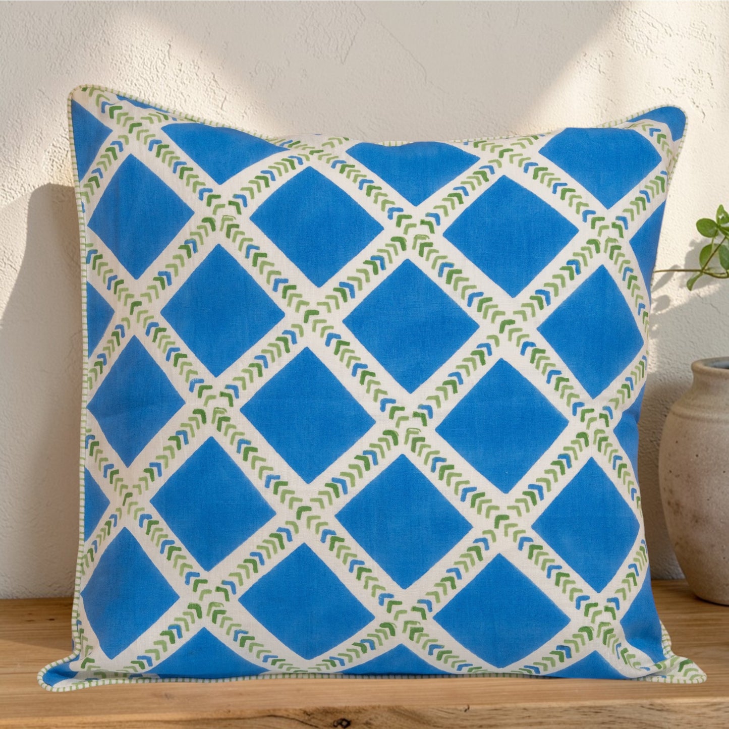 Hand block printed linen pillow cover with interlocking geometric green and blue chevron  print in natural dyes placed on a wooden surface