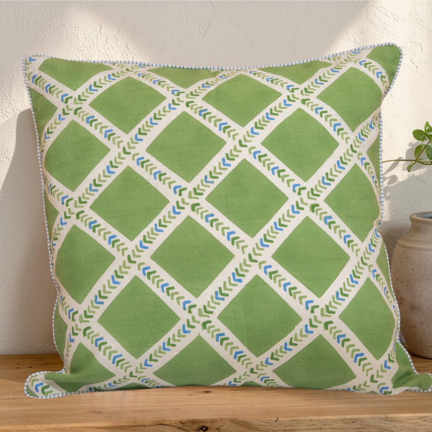 Hand block printed linen pillow cover with interlocking geometric green and blue chevron  print in natural dyes placed on a wooden surface with a neutral background