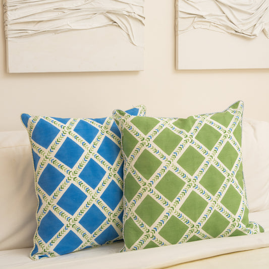 Two patterned pillows , Hand block printed linen pillow cover with interlocking geometric green and blue chevron  print in natural dyes placed on a  couch with a neutral background