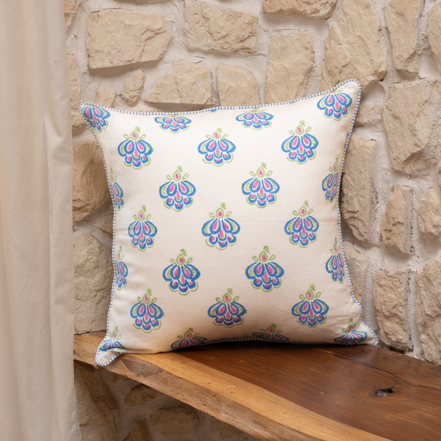 Peacock blue hand block printed linen pillow cover with intricate feather motif in natural dyes, styled on a stone wall background