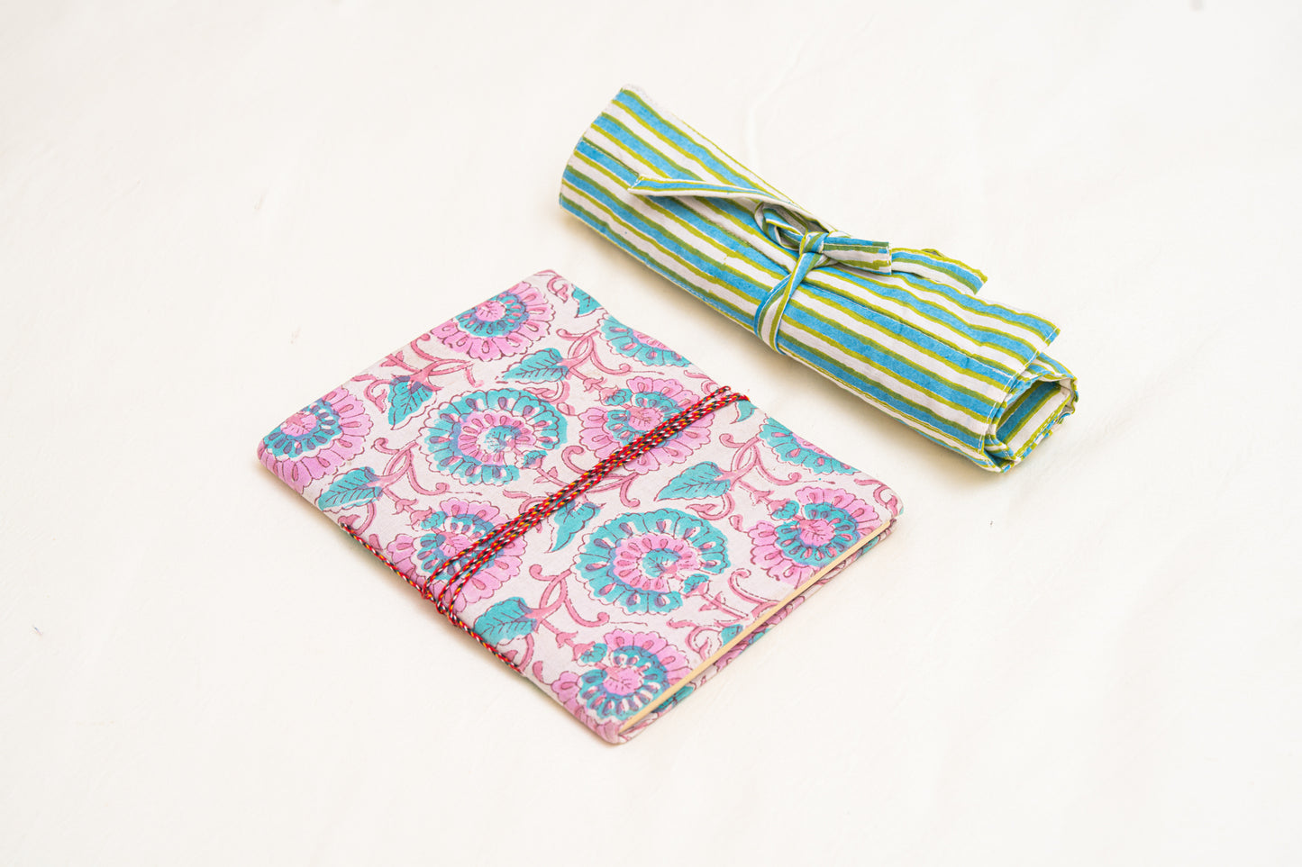 Pink and blue hand block printed fabric journal  with floral pattern and green striped cotton hand block printed  roll-up organizer  on a white background