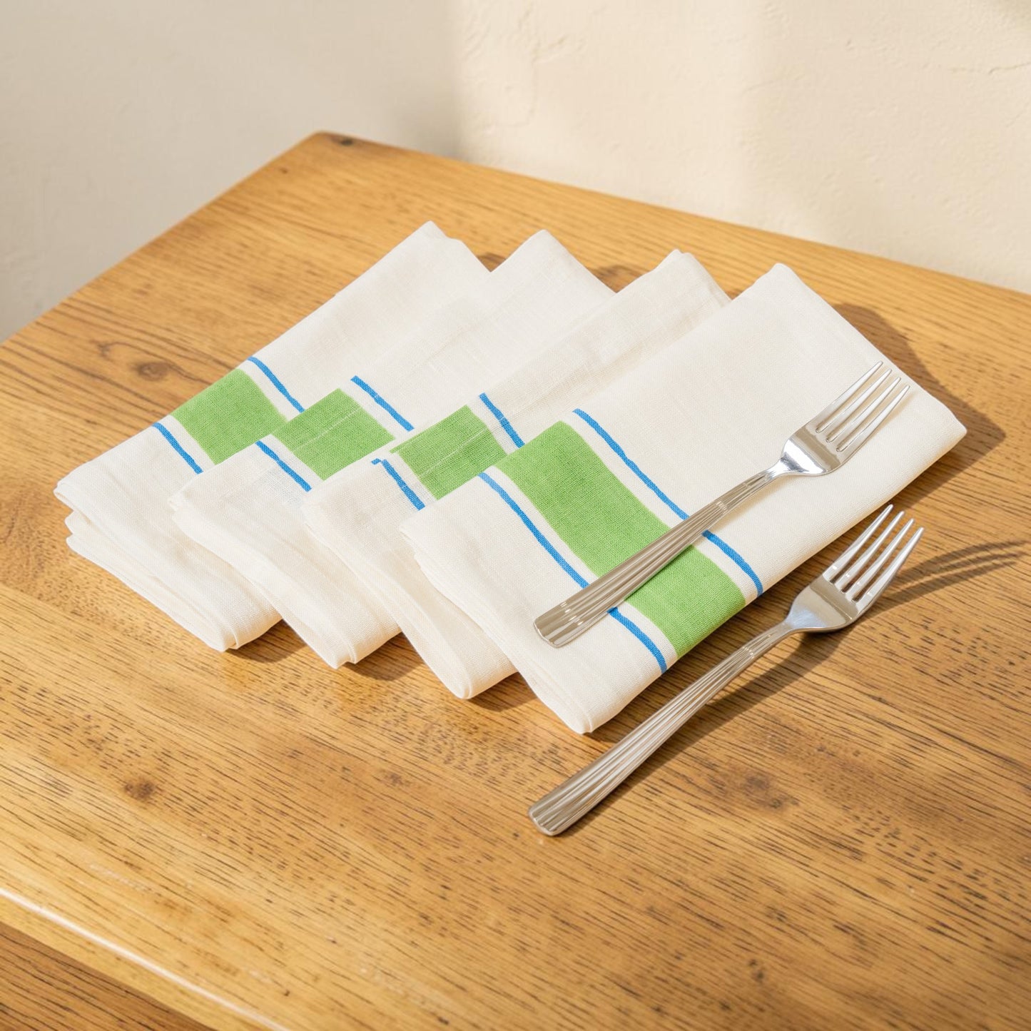 Set of white napkins with green and blue stripes hand block printed linen with natural dyes, on a wooden table with silver forks.