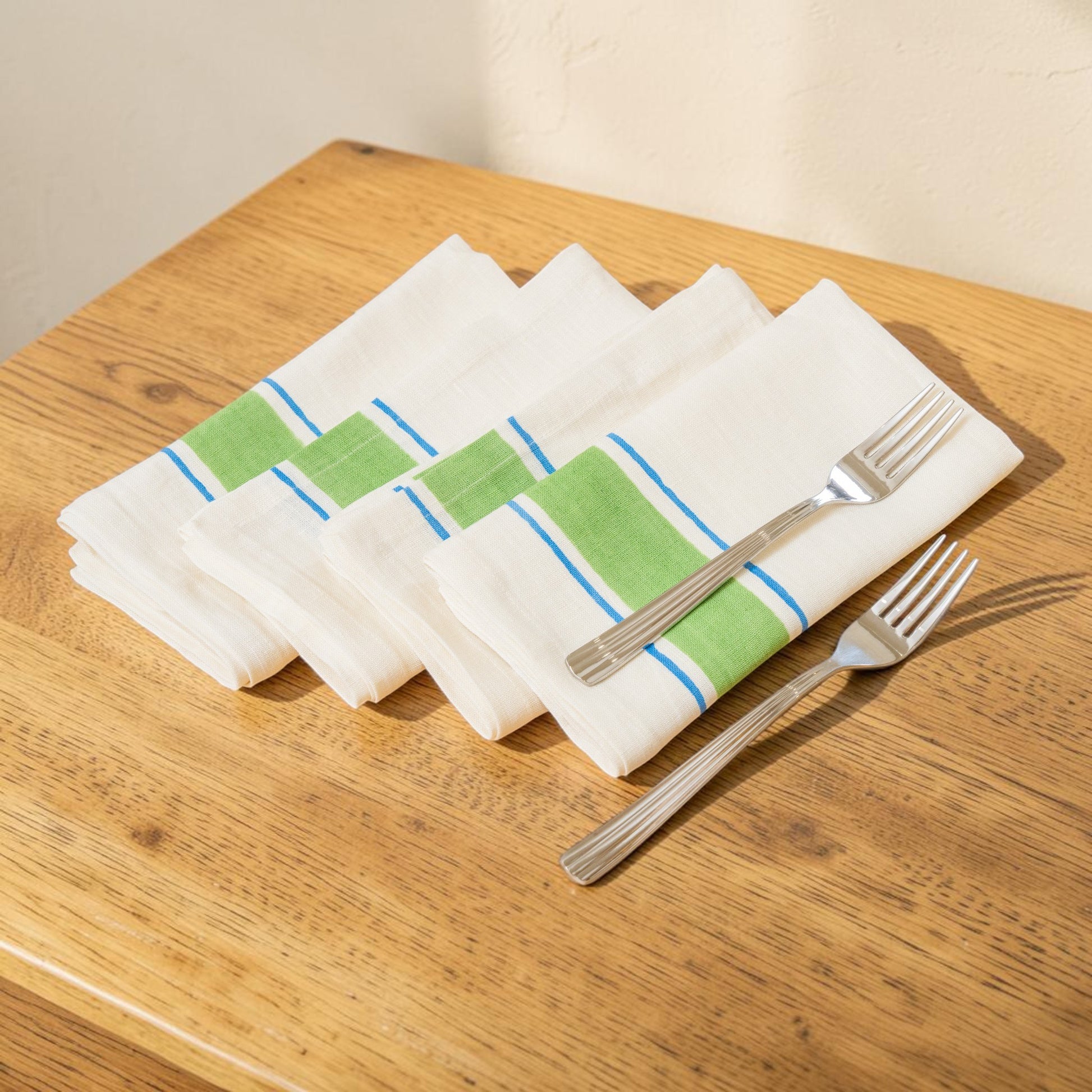 Set of white napkins with green and blue stripes hand block printed linen with natural dyes, on a wooden table with silver forks.