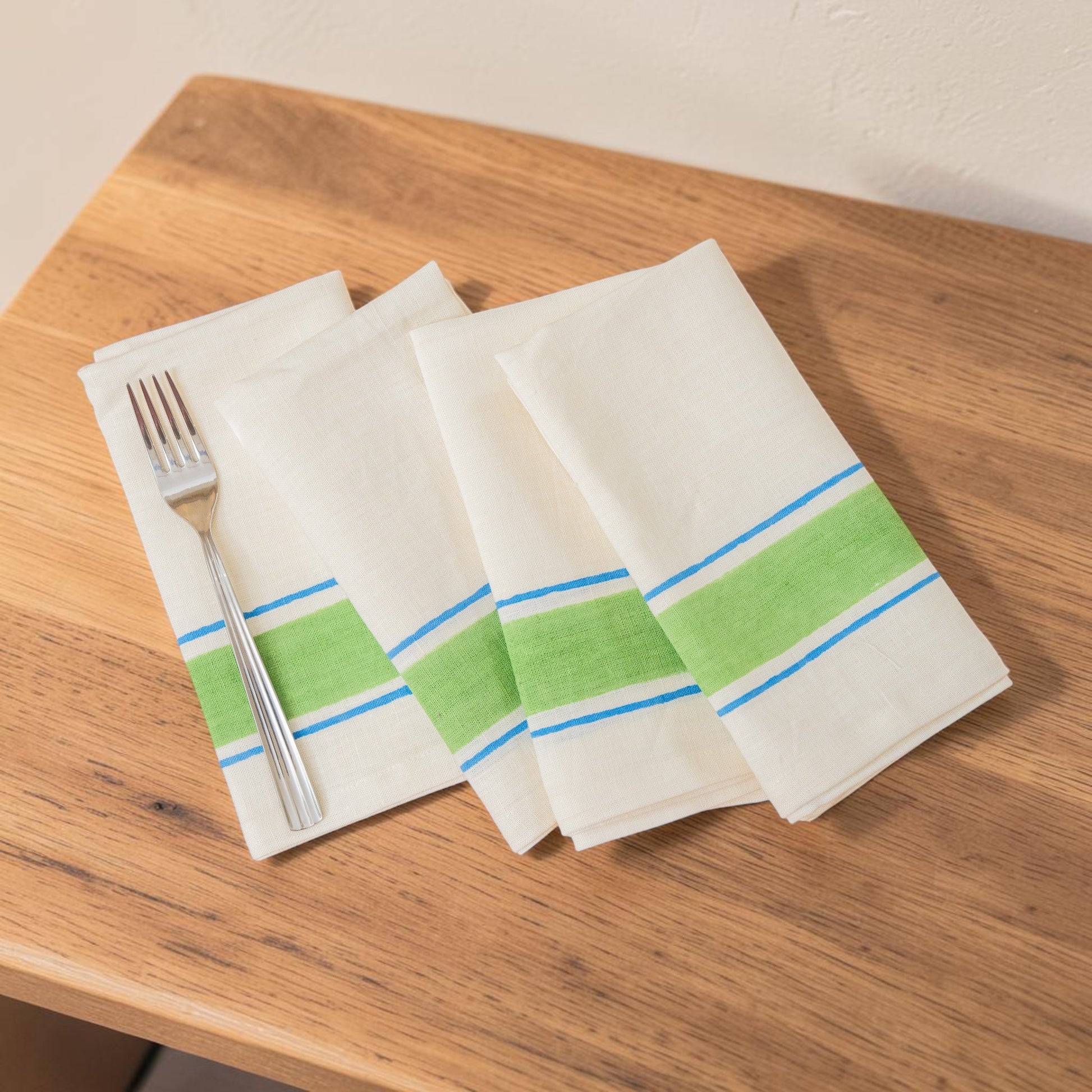 Set of four white napkins with green and blue stripes hand block printed linen, on a wooden surface.