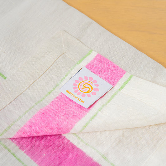 Hand printed linen napkins in pink, folded  with the peacock palette label laid out on a table